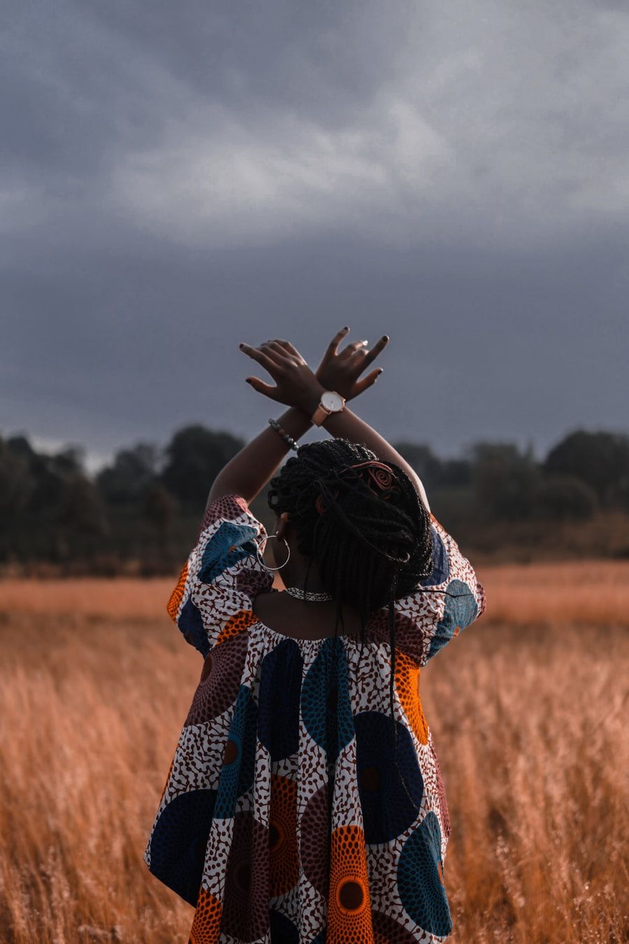 A woman in printed cloth standing in tall grass, arms raised